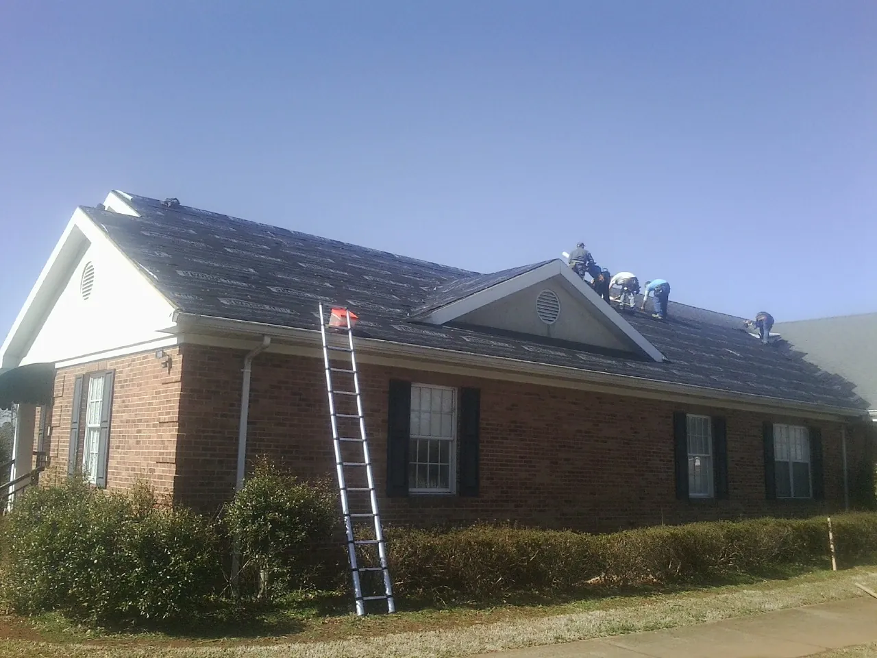 Crew tearing shingles off a brick ranch roof with a ladder set — Metal Roof Repair work by our crew in Gaylord