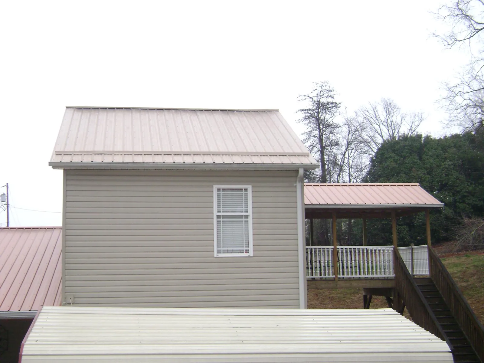 Tan metal roofs on a two story addition and attached porch, from a Roof Replacement job in Gaylord